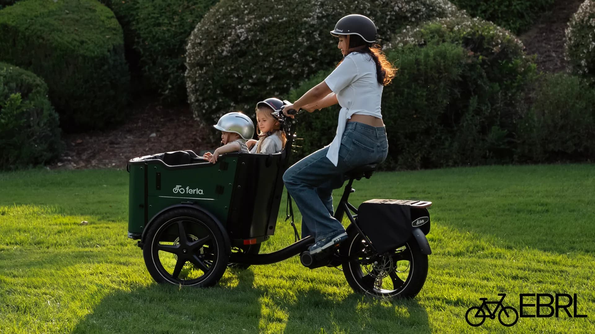 Rider on a Ferla Royce MAX cargo trike with two children in the green front box in a park