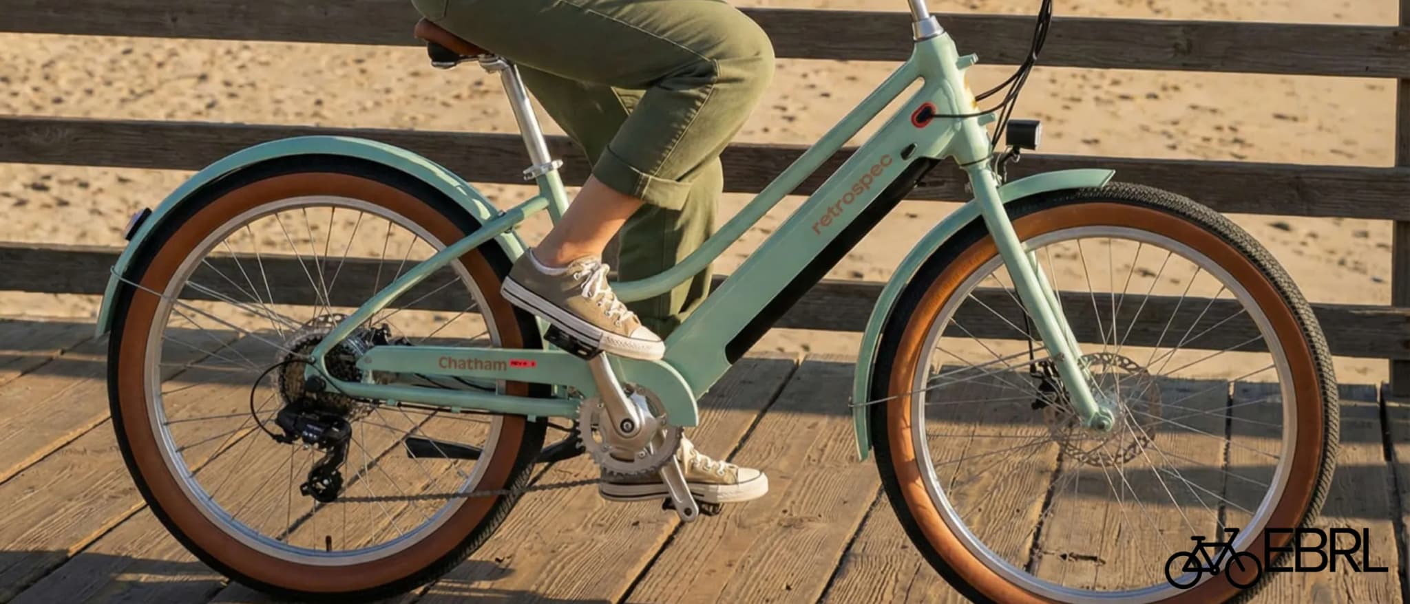 Retrospec Chatham Rev+ 2 Step-Through electric beach cruiser bike in Matcha green on a beachfront boardwalk