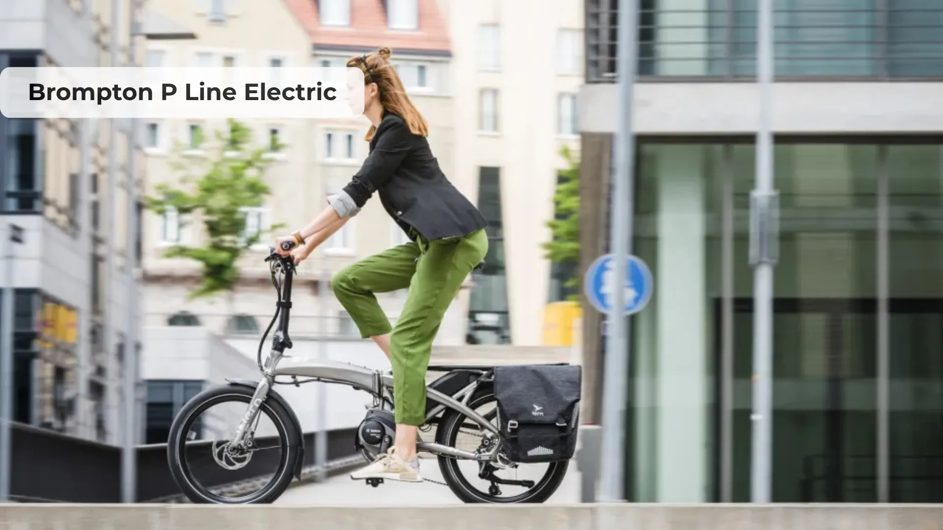 Brompton P Line Electric folding bike in titanium finish leaning against urban storefront